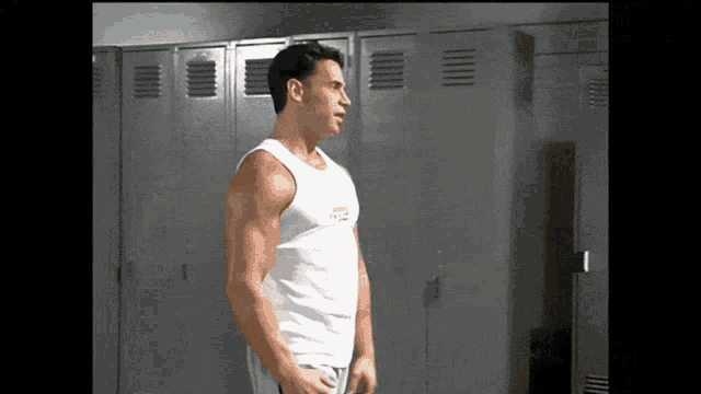 a man in a white tank top is standing in front of a row of lockers