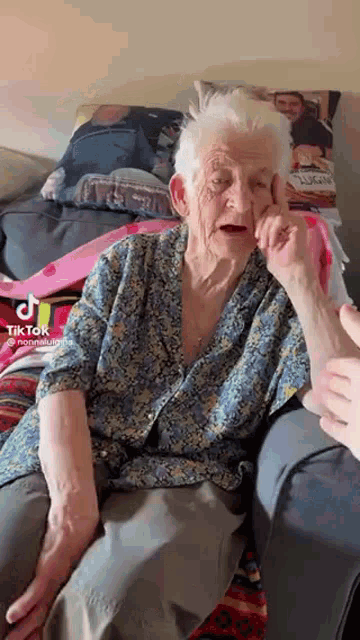 an elderly woman is sitting on a couch talking to a person .