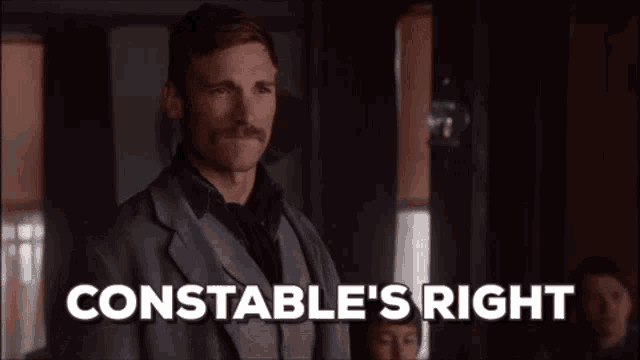 a man with a mustache is standing in front of a sign that says constable 's right ..