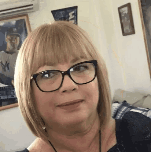 a woman wearing glasses is smiling in front of a picture of a baseball player