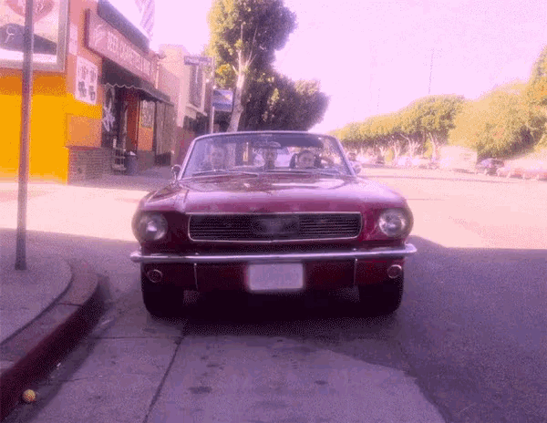 a red mustang is parked on the side of the road in front of a building that says beer