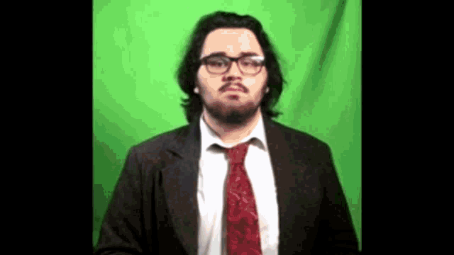 a man with glasses and a red tie is standing in front of a green background