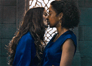 two women are kissing in front of a window while wearing blue clothes