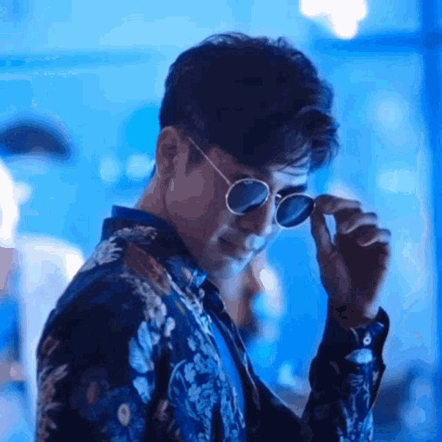 a man wearing sunglasses and a floral shirt is standing in a blue room .