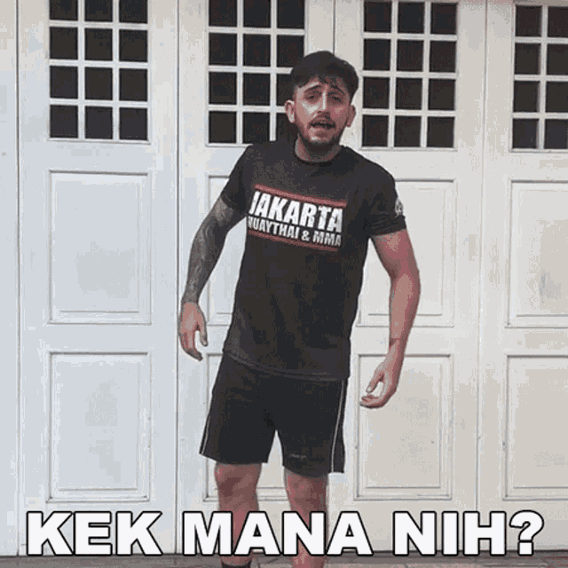 a man wearing a jakarta muaythai & mma shirt stands in front of a garage door