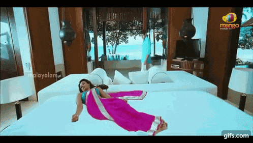 a woman in a pink saree is laying on a bed while a man stands behind her