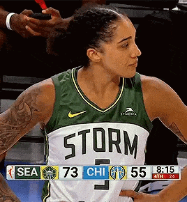 a female basketball player wearing a green and white storm jersey is standing on the court .