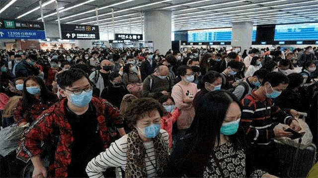 a large group of people wearing masks are standing in a crowded airport .