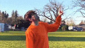 a man in an orange sweater is standing in a field pointing up