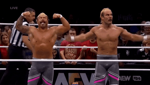 two men are flexing their muscles in a wrestling ring while a referee watches .