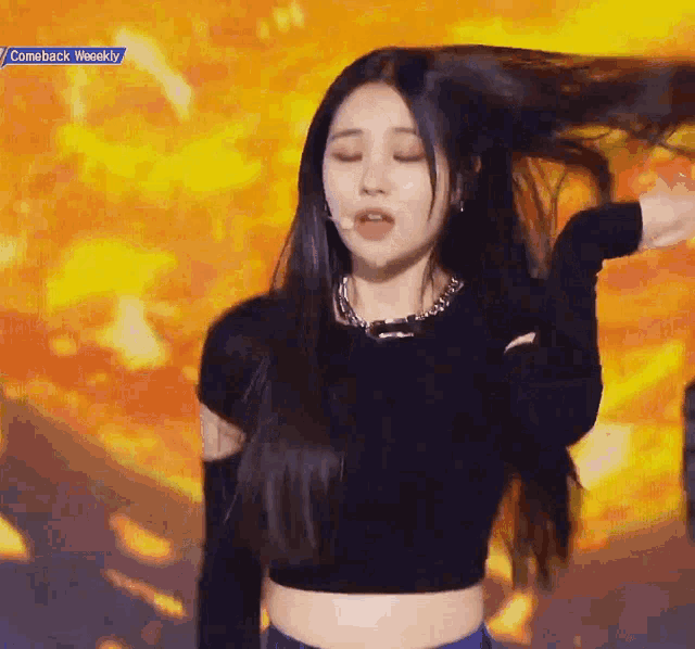 a woman in a black crop top is dancing with her hair in the air .