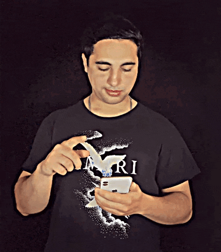 a man wearing a black shirt that says ari looks at his phone