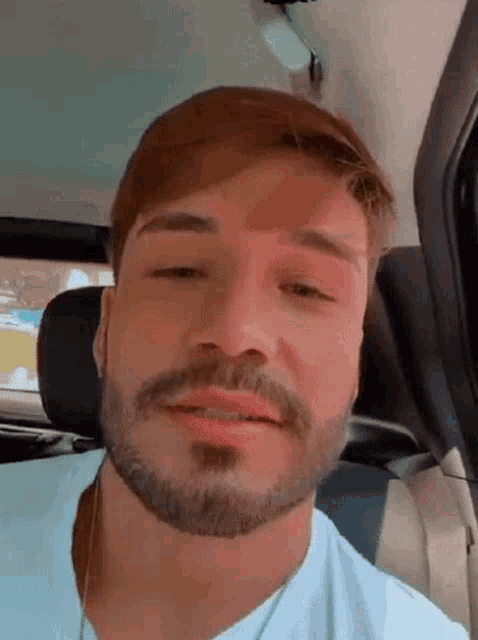 a man with a beard is sitting in the back seat of a car with his eyes closed .