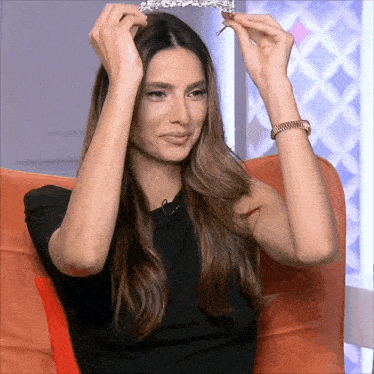 a woman wearing a black shirt is holding a tiara in her hands