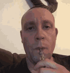 a man is smoking an electronic cigarette in front of a wall .