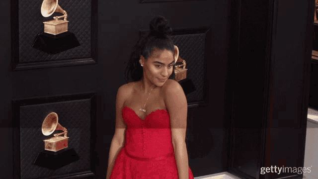 a woman in a red dress stands in front of a wall with grammophones