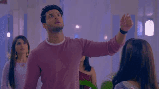 a man in a pink sweater is standing in a room with two women