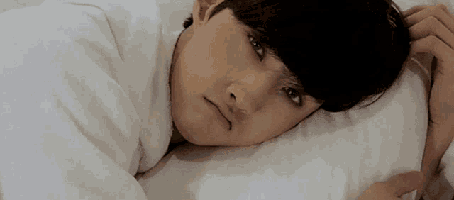 a young man is laying on a bed with his head on a pillow and looking at the camera .