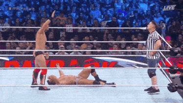 a referee is standing in a wrestling ring with two wrestlers in it .