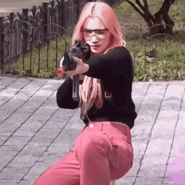 a woman with pink hair is holding a gun in her hand while wearing safety glasses .