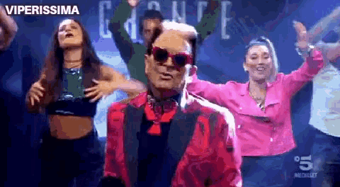 a man in a red jacket and sunglasses is dancing with a group of women