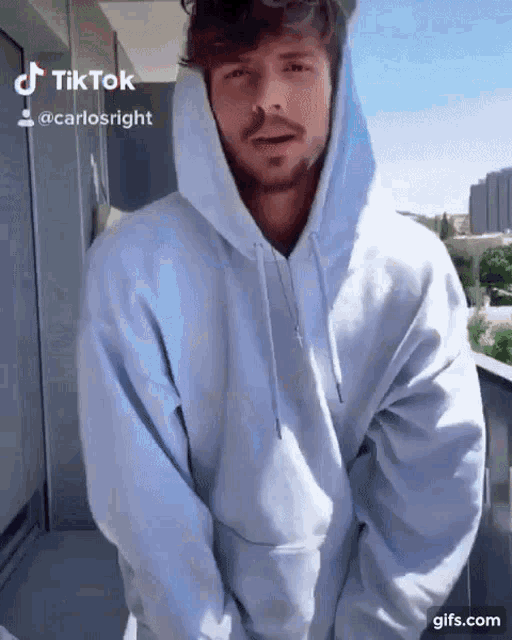 a man with a beard is wearing a white hoodie on a balcony ..