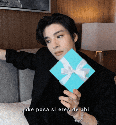 a man holding a blue gift box with the words " jake posa si eres de abi " written below him