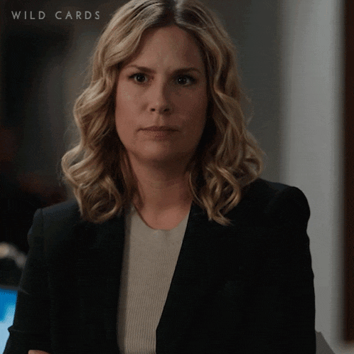 a woman in a black jacket stands with her arms crossed in front of a sign that says wild cards