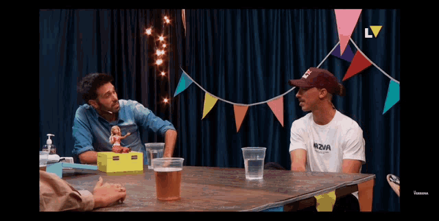 two men are sitting at a table and one of them is wearing a bbva t-shirt