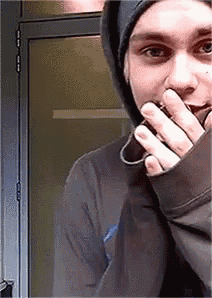 a man in a hooded jacket is covering his mouth with his hand .