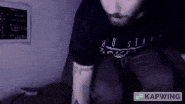 a man wearing a black shirt that says " no stay " sits on a couch