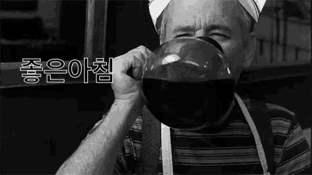 a black and white photo of a man drinking from a large bowl .