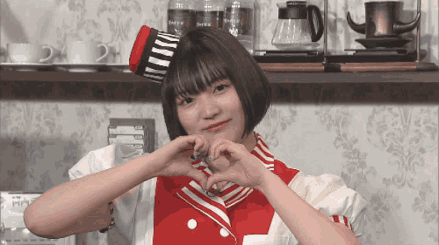 a girl in a red and white outfit making a heart sign
