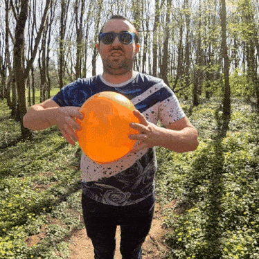 a man wearing sunglasses holds a large orange ball in his hands