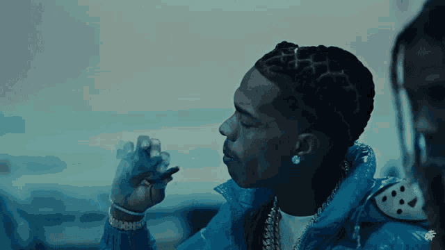a man in a blue jacket is smoking a cigarette and has the letter f on his earring