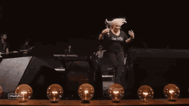 a woman in a black shirt that says come closer is jumping in the air on stage