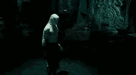 a man with long blonde hair is standing in the dark in a dark room .