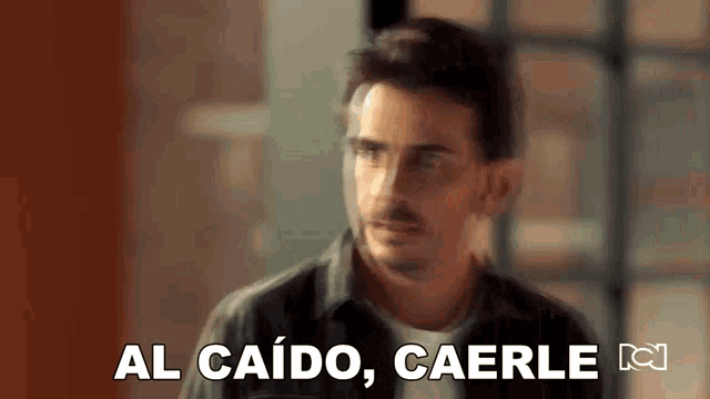 a man is standing in front of a window with the words `` al caido , caerle '' written on the screen .