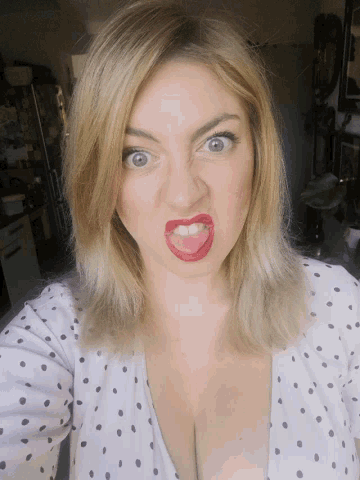 a woman wearing red lipstick and a polka dot shirt makes a face