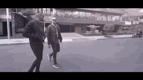 two men are walking down a street next to each other .