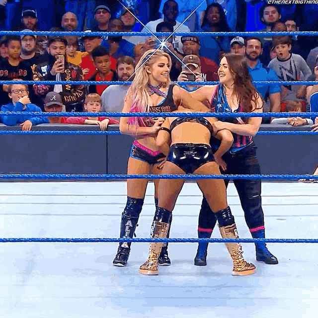 three women in a wrestling ring with one wearing a t-shirt that says ' the next thing '
