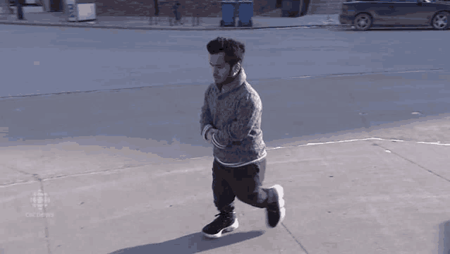 a man in a grey sweater and black pants is running on a sidewalk