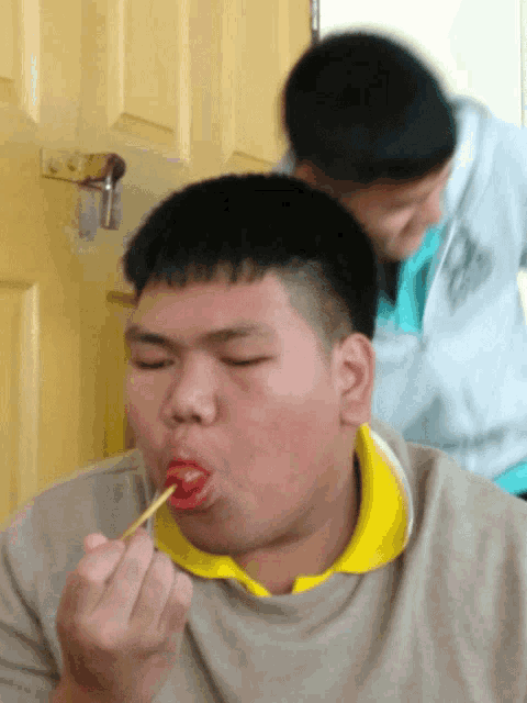 a man in a yellow shirt is eating something with a stick