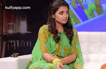 a woman in a green dress is sitting on a couch with her hands folded .