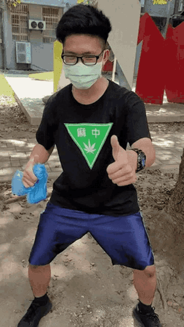 a man wearing a black shirt with a marijuana leaf on it gives a thumbs up