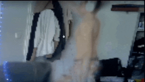 a blurry picture of a person standing in a room with clothes hanging on a wall .