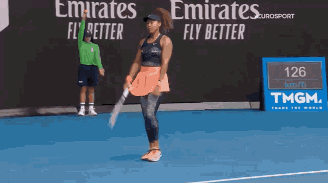 a woman is holding a tennis racquet on a tennis court in front of an emirates advertisement