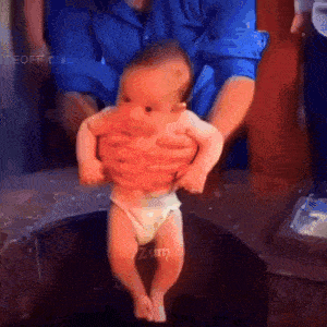 a baby in a diaper is being held by a man in a blue shirt with zum written on the bottom right