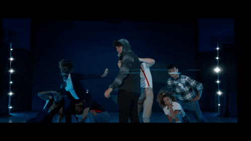 a group of people are dancing on a stage with a man in a hoodie holding a microphone