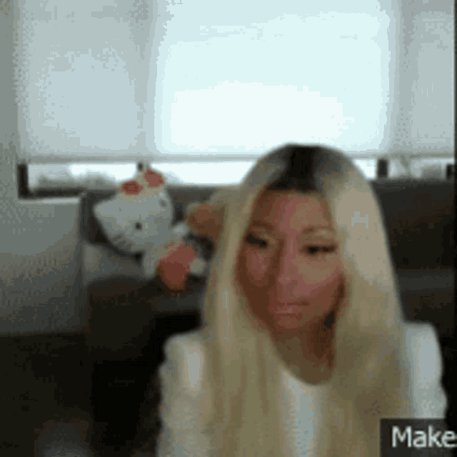 a woman with long blonde hair is sitting on a couch with a hello kitty stuffed animal .